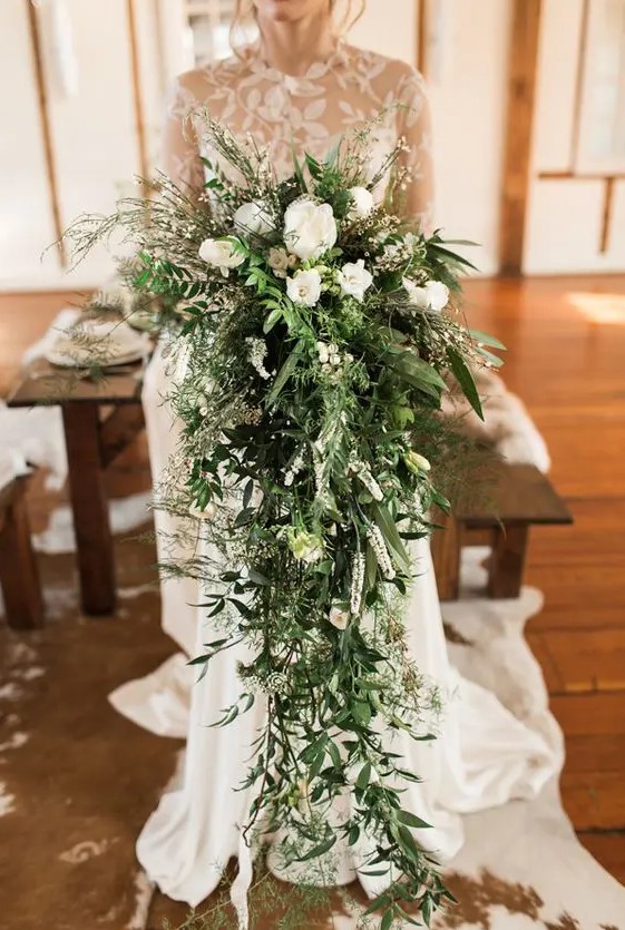 A jaw dropping cascading wedding bouquet of only white blooms and greenery that goes down to the floor is a gorgeous statement