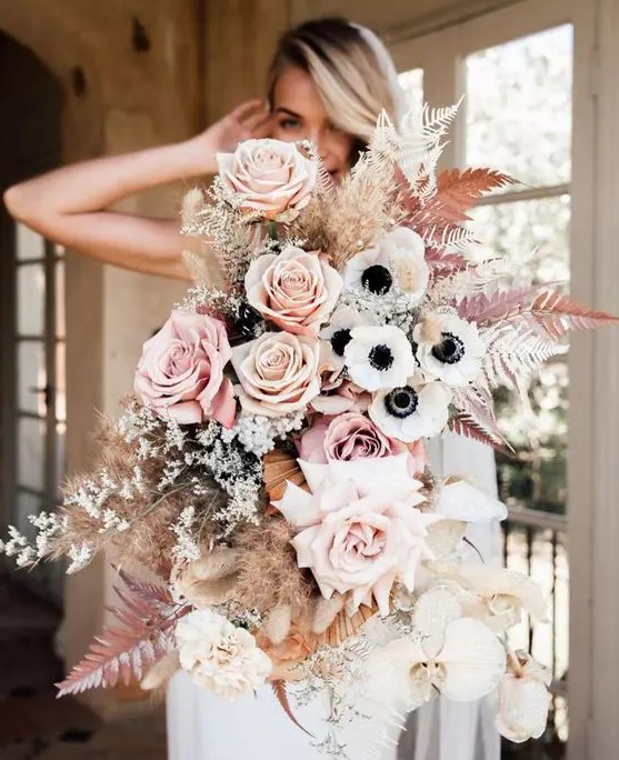 A jaw dropping wedding bouquet of blush and peachy pink roses, white anemones, orchids, spray painted ferns and grasses