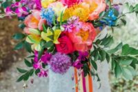 a jaw-dropping wedding bouquet of purple, pink, hot pink, yellow blooms and greenery and long colorful ribbon