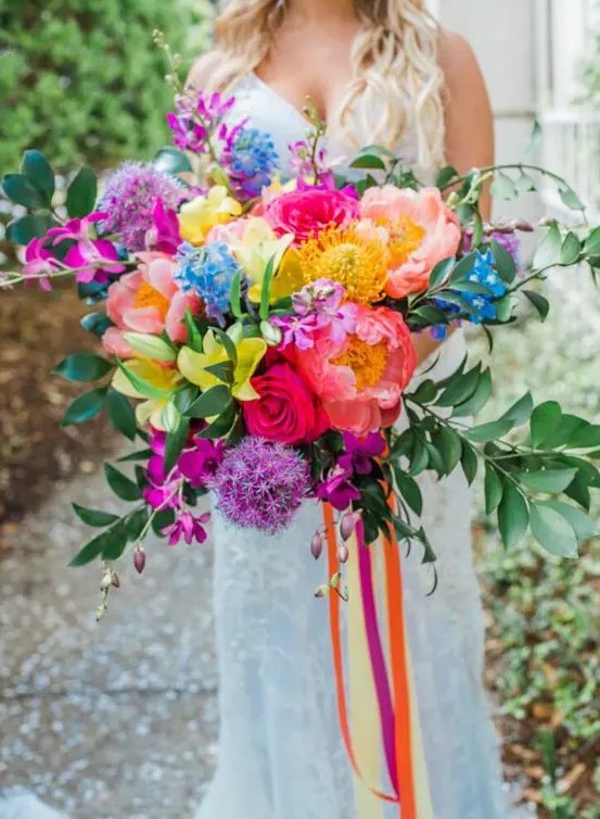 a jaw-dropping wedding bouquet of purple, pink, hot pink, yellow blooms and greenery and long colorful ribbon