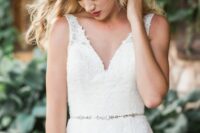 a lace semi-fitting wedding dress with no sleeves and a V-neckline plus a silver embellished sash are a stylish and catchy combo for a wedding