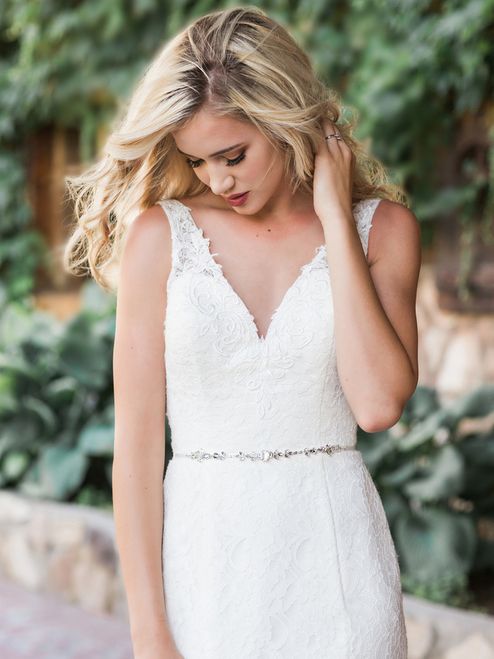 a lace semi fitting wedding dress with no sleeves and a V neckline plus a silver embellished sash are a stylish and catchy combo for a wedding