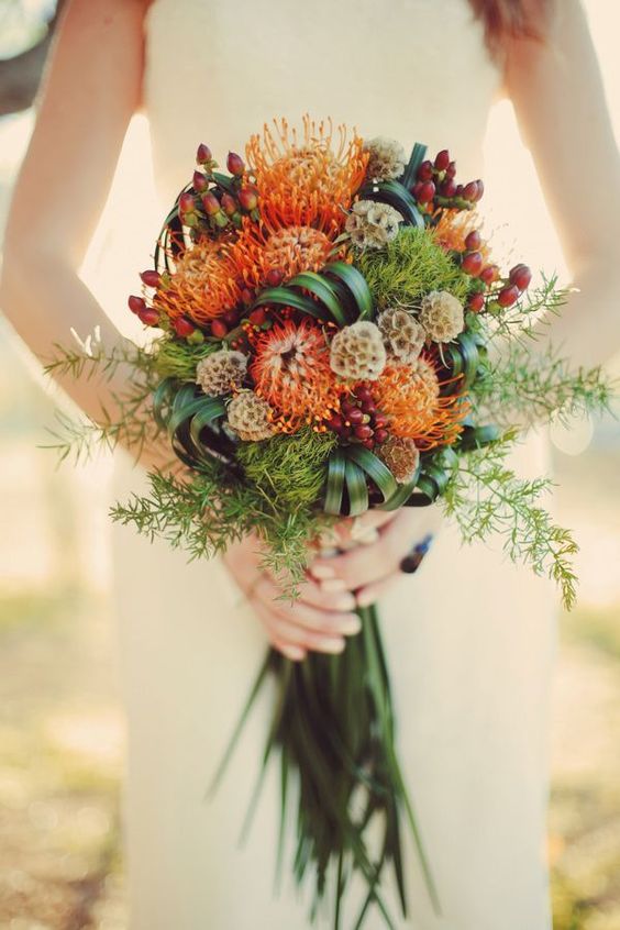 a long stem wedding bouquet of pincushion proteas, seed pods, greenery and grasses is a bold and cool idea for the fall and summer