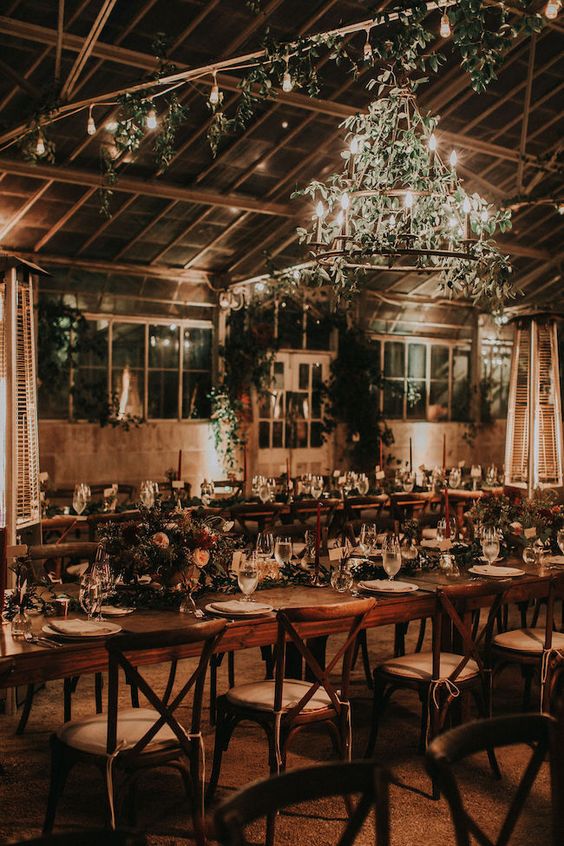 a lovely wedding venue lit up with string lights and a tiered chandelier, with lots of greenery is a very beautiful and cool idea