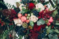a lush textural bouquet with red roses, privet berries, eucalyptus, pink flowers and red foliage