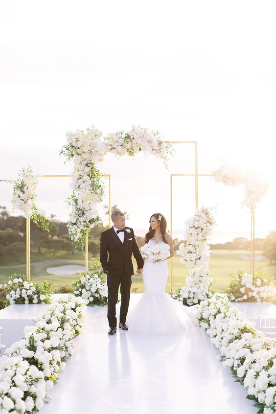 a lux modern wedding ceremony space with white floral lining up the aisle, simple arches with neutral blooms