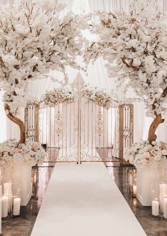 a luxurious wedding ceremony space wiht blooming trees, floral arrangements and pillar candles plus a gate