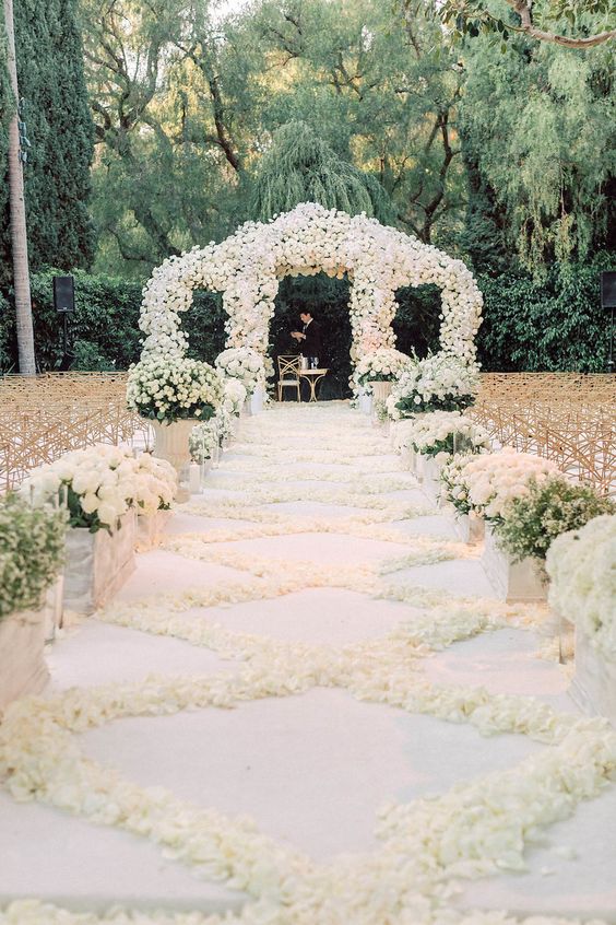 a luxurious wedding ceremony space with a lush white floral arch, a white petal pattern on the floor, white floral arrangements