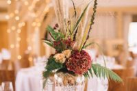 a mercury glass vase on a wood slice, bright blooms, greenery and pampas grass plus berries for a barn wedding