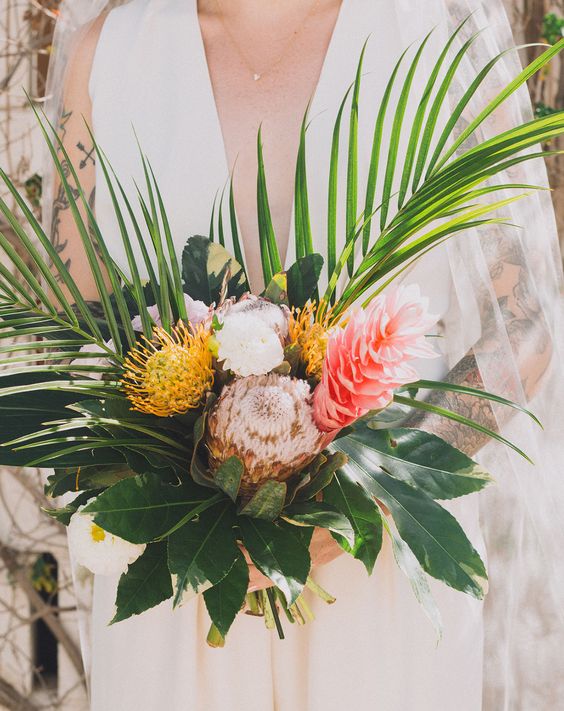 a minimalist tropical wedding bouquet of white and pink blooms, pincushion and king proteas, leaves and foliage is a cool idea to rock