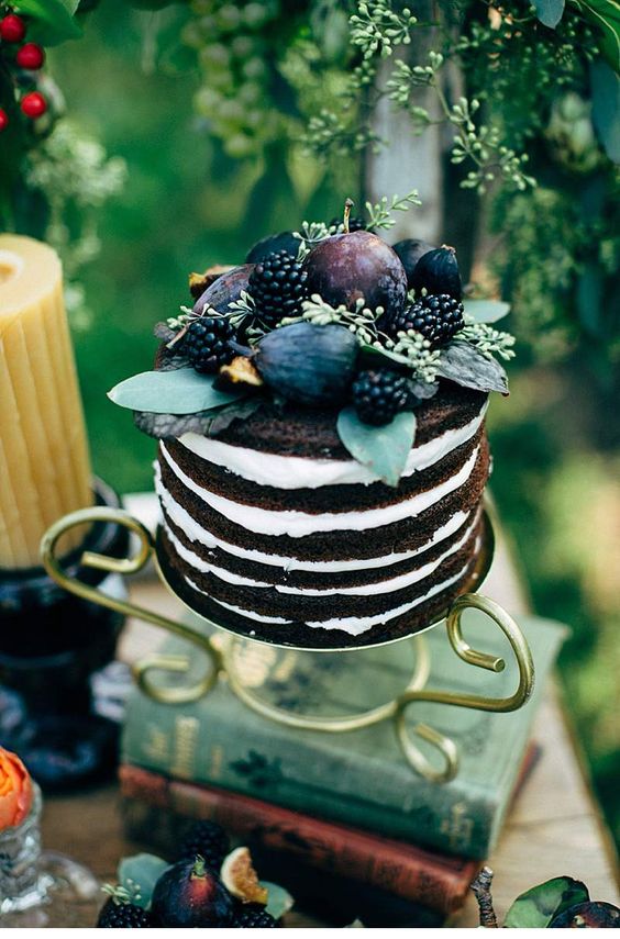 a naked chocolate wedding cake topped with fresh fruit and berries, with greenery is a fantastic and yummy-looking idea for a fall wedding
