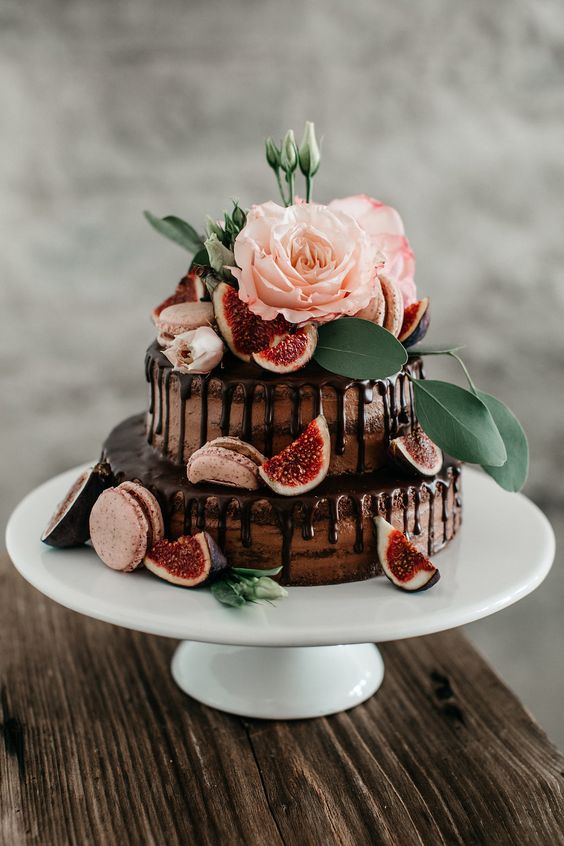 a naked chocolate wedding cake with chocolate drip, pink macarons, blooms, greenery and fresh figs is a delicious-looking and lovely idea for a wedding