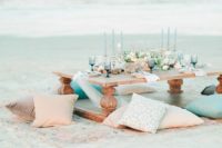 a pastel beach bridal shower with a low table, pastel pillows, blue glasses and candles plus neutral blooms