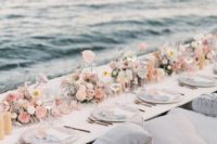 a pastel coastal wedding picnic table with pastel blooms, candles, neutral plates and lots of pillows
