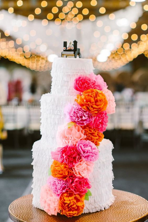 a pretty cake-shaped fringe pinata with colorful paper blooms is a gorgeous idea of an alternative wedding guest book