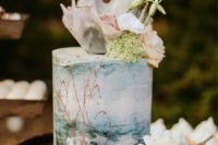a pretty watercolor painted cake with seashells, pink blooms and greenery for a beach bridal shower