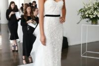 a refined lace fitting strapless wedding dress with ruffles on the back and a black sash, statement earrings by Marchesa