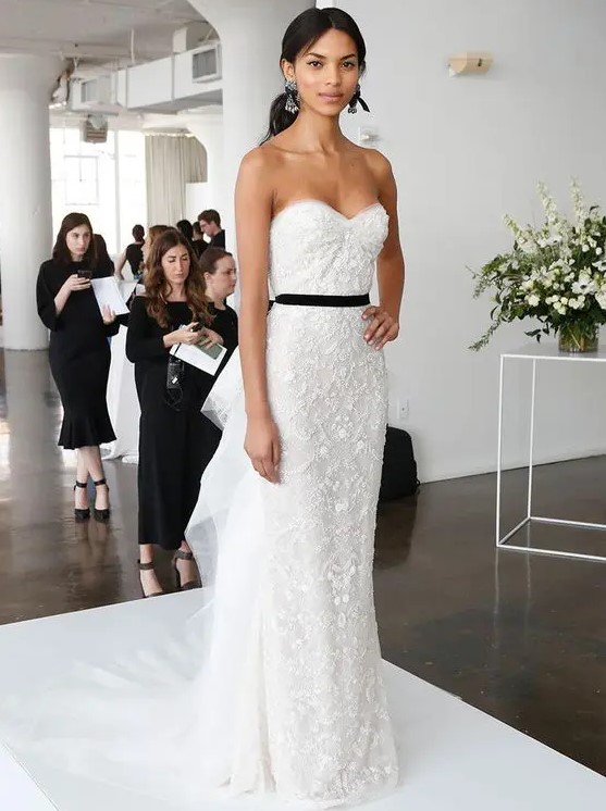 a refined lace fitting strapless wedding dress with ruffles on the back and a black sash, statement earrings by Marchesa