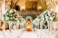 a refined wedding ceremony space with floral arrangements and greenery in tall clear vases, with a lush floral arch and candles