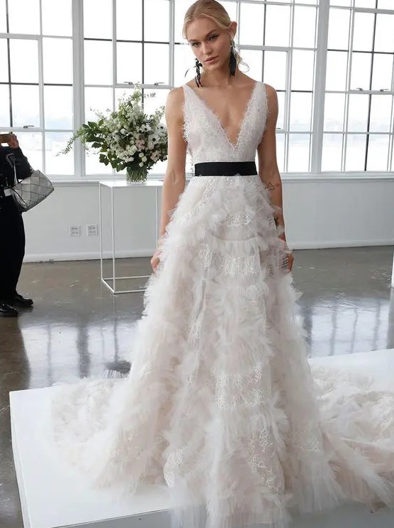 a romantic lace A line wedding dress with a plunging neckline, no sleeves, a black sash for an accent and black earrings by Marchesa