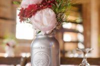 a simple and cute barn wedding centerpiece of a wood slice, a silver jar with greenery, pink and red blooms