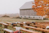 a simple and lovely outdoor barn wedding ceremony space with a large living tree, lots of fall leaves under it, wooden benches and bright blankets