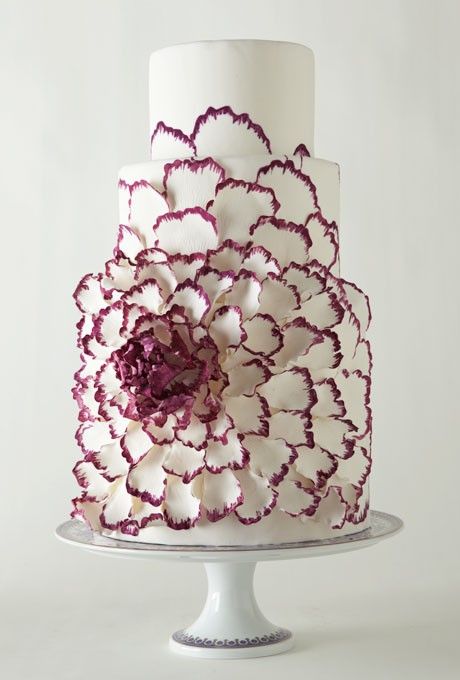 a sleek white wedding cake with an oversized white flower with pink edges is a stylish and bright idea for a modern wedding