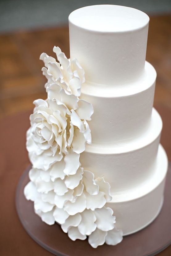 a sleek white wedding cake with an oversized white sugar flower as decor is a stylish idea for a modern wedding