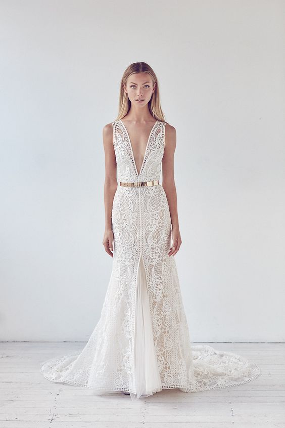 a sophisticated boho lace mermaid wedding dress with a plunging neckline and no sleeves plus a train and a shiny gold metallic belt