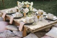 a stylish and refined wedding picnic with a low table, pillows, shiny chargers, neutral blooms and candles
