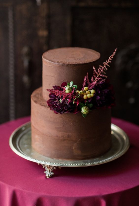 a stylish chocolate wedding cake with deep burgundy blooms, berries and a blooming branch for a refined and dark-colored fall wedding