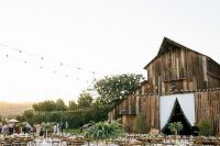 a stylish modern outdoor barn wedding reception with square tables and greenery arrangements, with white linens and greenery around is cool