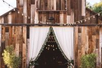 a stylish outdoor barn wedding reception with long tables, greenery arrangements, string lights and neutral linens is a chic idea