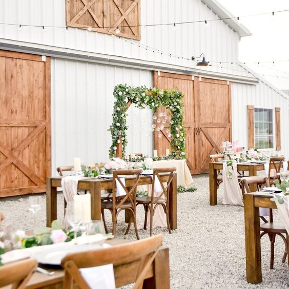 a stylish outdoor barn wedding reception with stained furniture, neutral textiles and neutral and pastel florals plus greenery