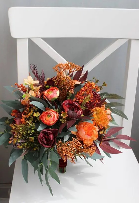 a super bold wedding bouquet of orange ranunculus, peonies, pincushion proteas, dark blooms, greenery, dark foliage and a bit of berries
