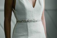a textural fitting wedding dress wiht a deep V-neckline and no sleeves plus a chic white bead belt is a lovely idea for a modern wedding