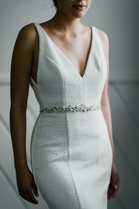 a textural fitting wedding dress wiht a deep V neckline and no sleeves plus a chic white bead belt is a lovely idea for a modern wedding