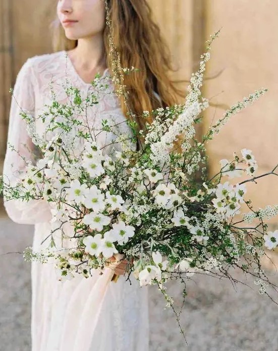 A unique spring like wedding bouquet of various kinds of blooms and greenery looks wild