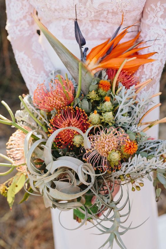 a unique wedding bouquet of air plants, pincushion proteas, seed pods, bold orange blooms and greenery is amazing
