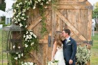 a vintage barn door wedding backdrop with greenery and white florals is a chic and beautiful idea for a barn wedding