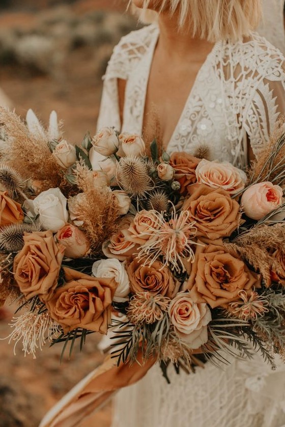 A warm colored rust wedding bouquet with white blooms, dried touches and greenery for a desert boho bride