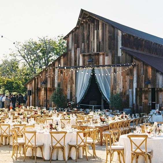 a welcoming outdoor barn wedding reception with round tables and stained chairs, string lights and bold blooms is a cool space