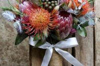 a whimsical wedding bouquet of king and pincushion proteas, pale leaves and greenery, a twine wrap and a bow of ribbon