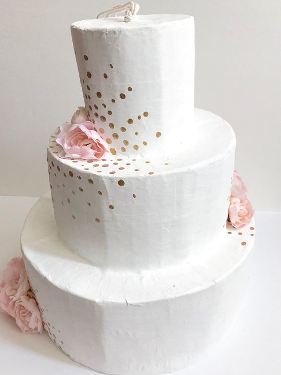 a white wedding cake pinata with gold polka dots and pink paper blooms is a lovely idea of a wedding guest book