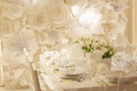 a white wedding reception with oversized white blooms on the wall and matching white blooms on the table