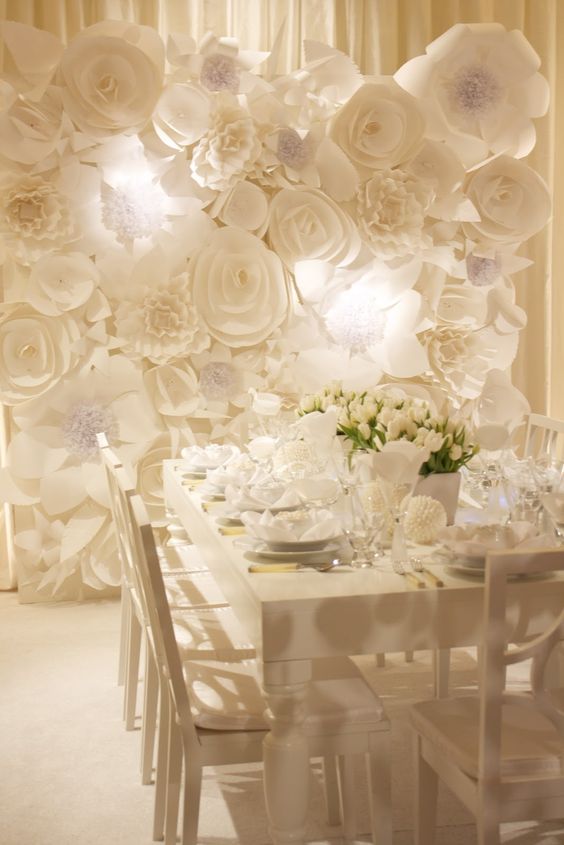 a white wedding reception with oversized white blooms on the wall and matching white blooms on the table