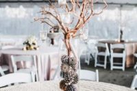 a winter barn wedding centerpiece of candles, a clear vase with pinecones and branches with candles hanging on them