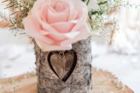 a wood slice with a bark wrapped vase, baby’s breath, greenery and a pink rose is a great barn centerpiece