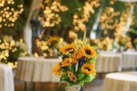 a wood slice with a candle lantern, a lace wrapped jar with greenery and sunflowers for a summer or fall barn wedding
