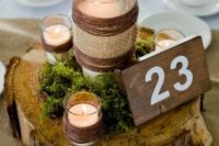 a wood slice with moss, candles wrapped with twine, a tall candle wrapped with twine and burlap and a table number